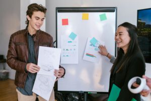 A man and a woman working for a tech startup are presenting a pitch deck to a group of investors, showcasing slides with data and visual aids in a modern office setting.